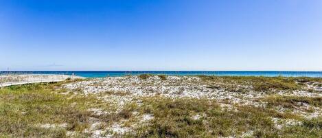 Une plage avec une promenade en bois qui mène à l’eau, des dunes de sable et un ciel bleu dégagé.