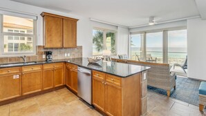 A kitchen with wooden cabinets, a black countertop, and a view of the beach. - BC 201A Beach Club 2B Gulf Front w/Daily Beach Chair Set! (Pensacola Beach)