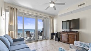 A living room with a sofa, a television, and a view of the ocean through large glass doors. - BC 202A Gulf Front with Daily Beach Chair Set! (Pensacola Beach)