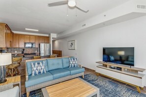 Una sala de estar moderna con sofá, televisión y una cocina al fondo.