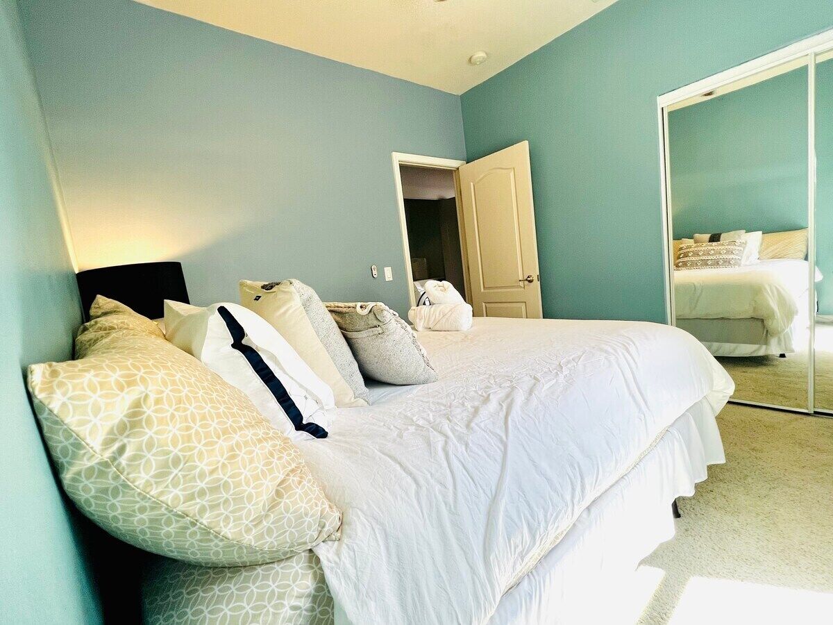 A bedroom with a bed, pillows, a nightstand, and a door leading to another room.