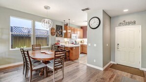 Een moderne keuken met houten kasten, een centraal eiland, hangende lampen en een eethoek met een houten tafel en stoelen.