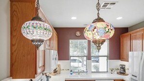 Een keuken met houten kastjes, een fornuis en twee hangende decoratieve lampen.