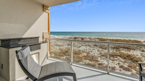 A balcony with a view of the beach, a seating area with a table, and a small kitchen area. - 1B Gulf Front*Beach Chairs*Beach Club! (Pensacola Beach)