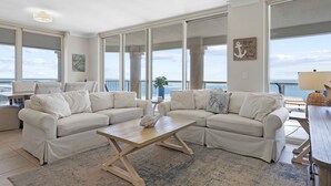 Ein geräumiges Wohnzimmer mit einer großen Eckcouch, einem Holztisch und Blick auf den Ozean durch große Fenster.