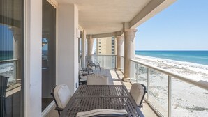 Varanda com mesa e cadeiras, vista para uma praia e para a paisagem urbana.