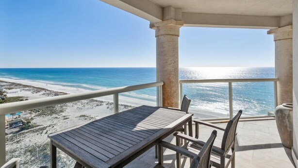 Een balkon met een tafel en stoelen met uitzicht op een strand en de oceaan.