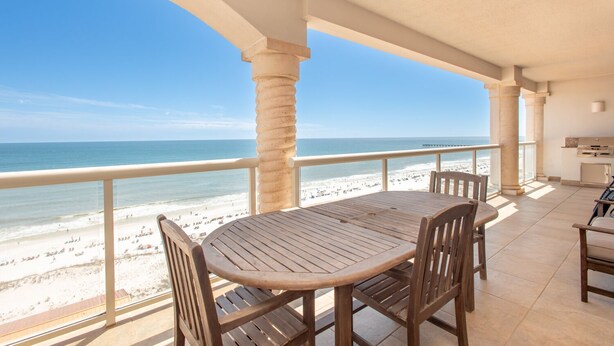 Un espace extérieur abrité, doté d’une table et de chaises en bois, qui offre une vue sur une plage et un ponton.