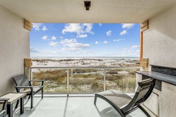 A balcony with a view of the beach, a table, two chairs, and a bar counter.