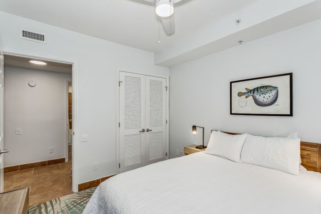 A bedroom with a bed, a nightstand, a framed picture on the wall, and a door leading to another room.