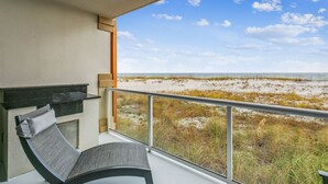 Un balcón con vistas a la playa, una zona de estar con una silla acolchada y una mesita.