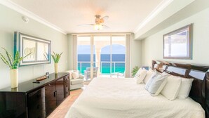 A spacious bedroom with a large bed, a desk, and a chair. There is a balcony with a view of the ocean. - Dly Beach Chairs! -Beach Club 3B Gulf Front @ Pensacola Bch (Pensacola Beach)