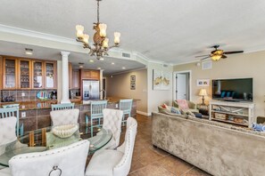 A spacious living area with a dining table, chairs, a sofa, a TV, and a kitchen in the background.