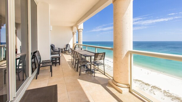 Un espace extérieur abrité, doté d’une table et de chaises, qui offre une vue sur une plage aux eaux d’un bleu cristallin.