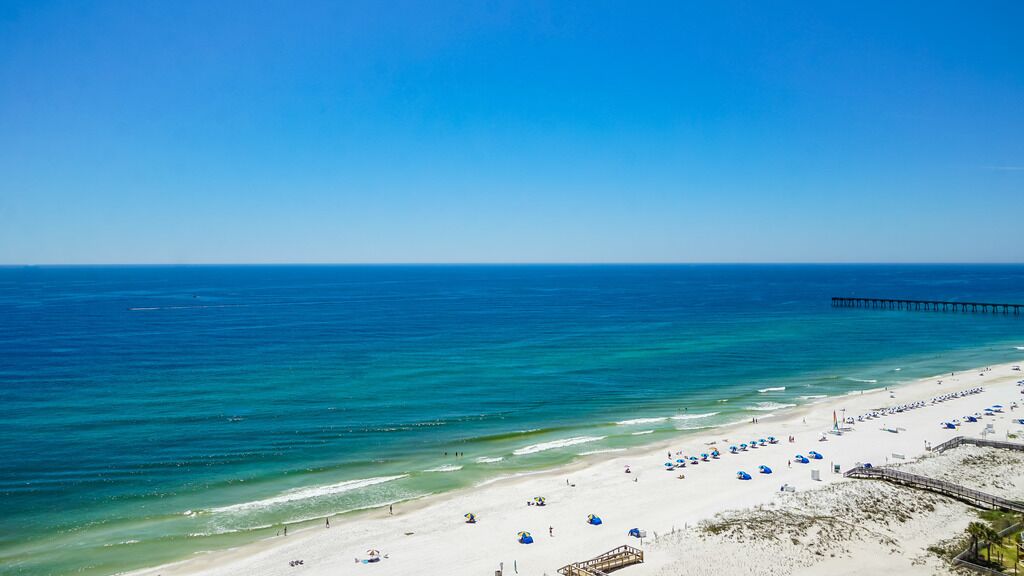 A beach with a pier extending into the ocean, sandy beach, and umbrellas.
