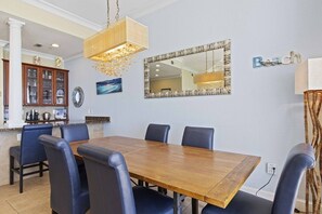 Un comedor con una mesa de madera y sillas azules, un espejo grande y un mueble con puertas de vidrio.
