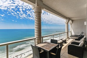 Ein Balkon mit Korbmöbeln mit Blick auf einen Strand und den Ozean.