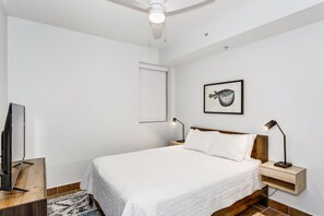 A bedroom with a bed, a television, a ceiling fan, a framed picture, and bedside lamps. - BC 204B 1B Gulf Front - Daily Beach Chair Set! (Pensacola Beach)