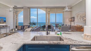 A modern kitchen with a large island, a dining area with a view, and a living space with a sofa and a TV. - 3B Beach Club Penthouse BC 2104 - Daily Beach Chair Set! (Pensacola Beach)
