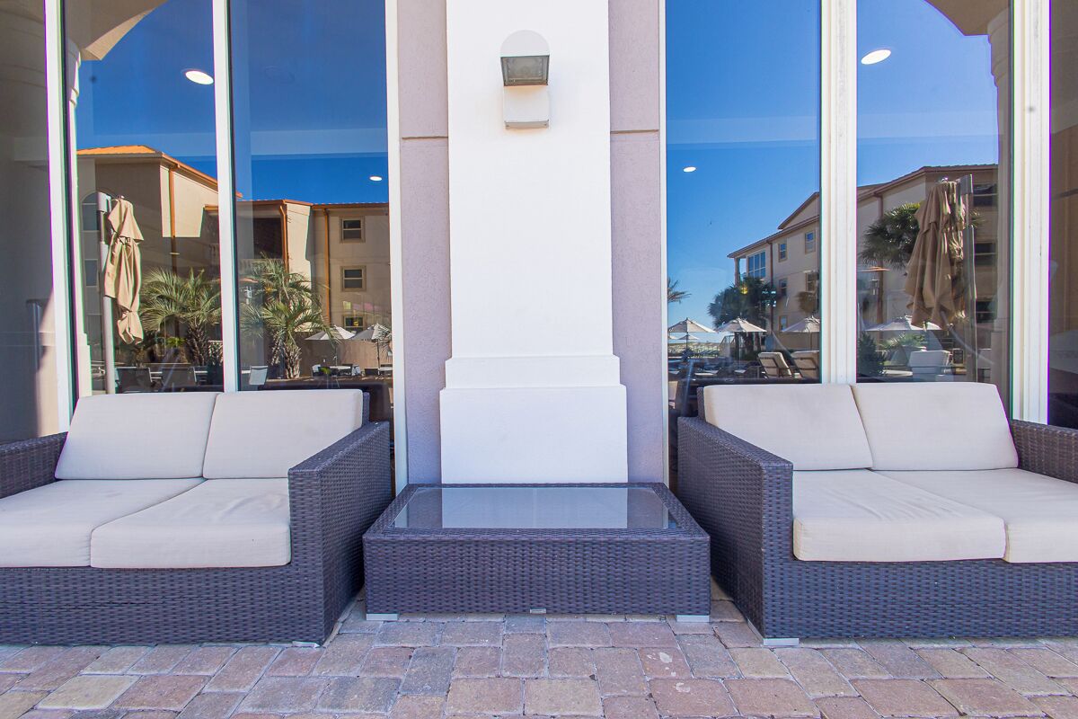 A modern outdoor seating area with wicker furniture and a glass table, surrounded by large windows.
