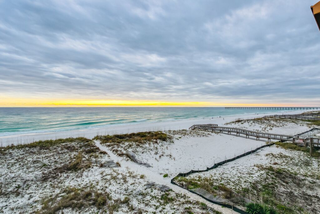 A beach with a wooden boardwalk, sandy dunes, and a pier extending into the ocean.