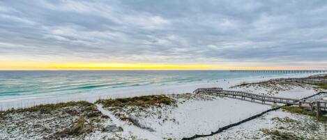A beach with a wooden boardwalk, sandy dunes, and a pier extending into the ocean.
