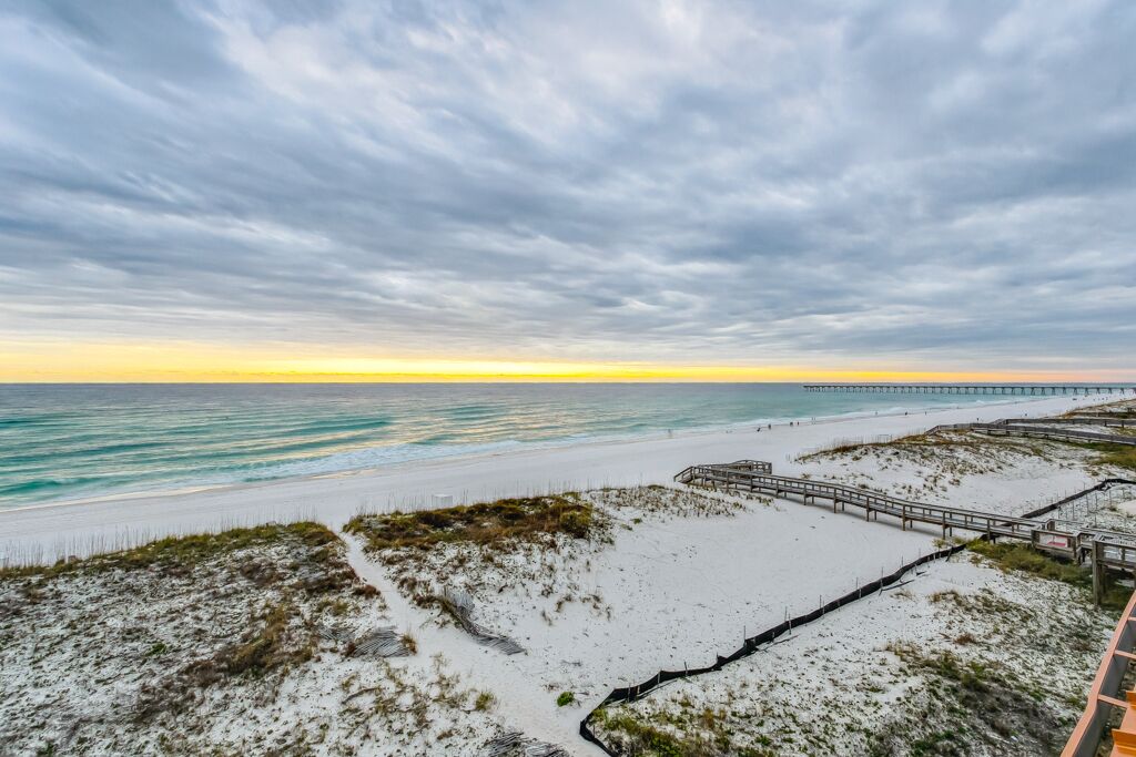 A beach with a wooden boardwalk, sandy dunes, and a pier extending into the ocean.