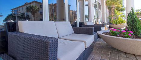 A wicker sofa with cushions, a potted plant with pink flowers, and a brick patio.