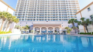 A hotel with a large pool, a multi-story building, and palm trees.