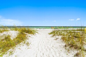 A sandy beach path leading to the ocean with beach umbrellas and people in the distance.