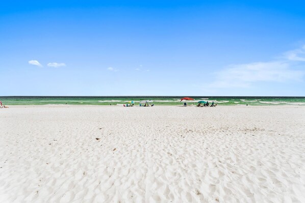 A wide sandy beach with a few umbrellas and beach chairs.