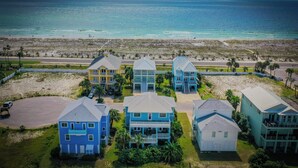 A coastal residential area with multiple two-story houses, a beach in the background, and a road leading to the beach.