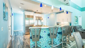 A modern kitchen with a central island, bar stools, and a dining area.