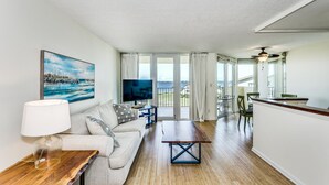 A modern living room with a sofa, TV, and dining area. - Beach and Bay Views at Santa Rosa Dunes! (Pensacola Beach)