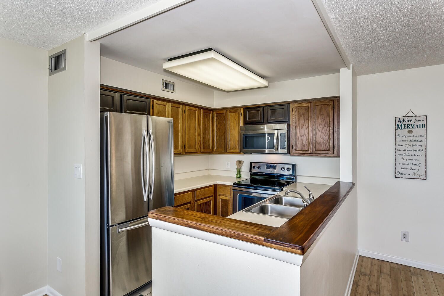 Cocina compacta con armarios de madera, electrodomésticos de acero inoxidable y encimera de madera.