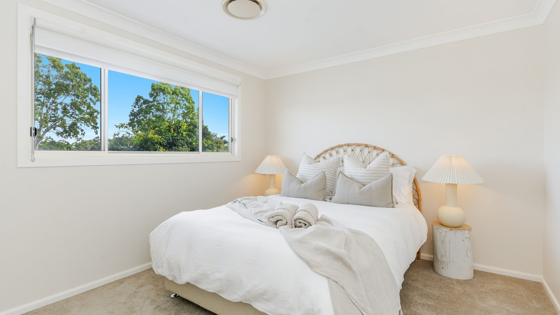 A bedroom with a large bed, two bedside lamps, a window with a view of trees, and a ceiling light.