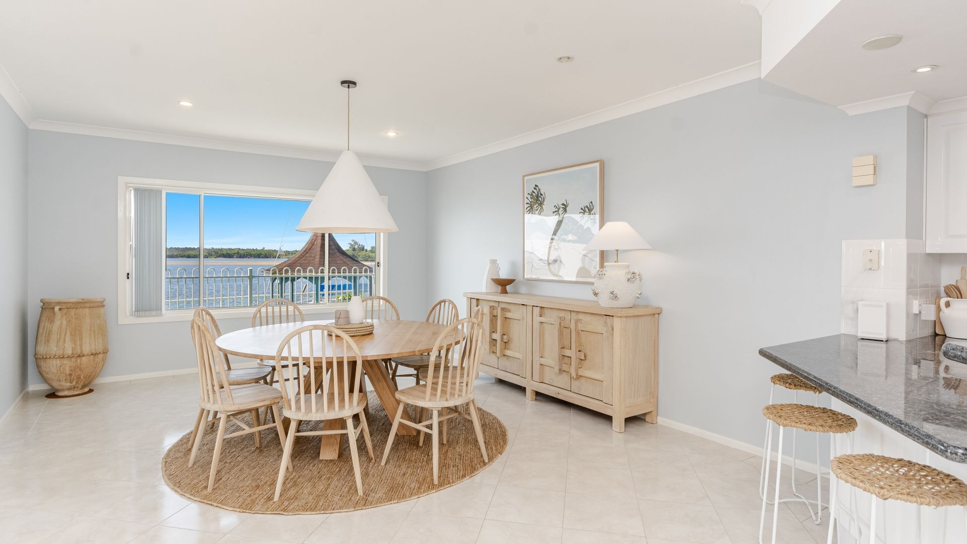 A spacious kitchen with a dining area, large windows with a view of the water, and a modern light fixture.