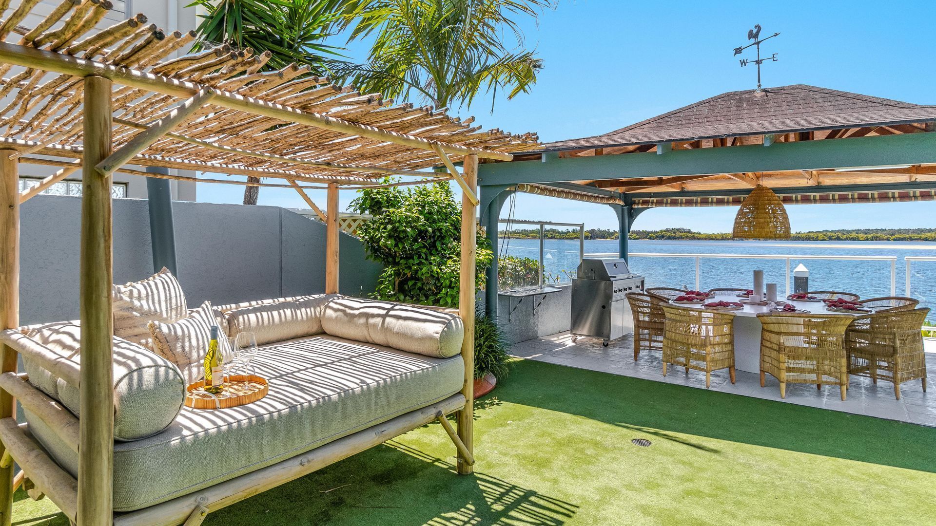 A covered outdoor seating area with a sofa and dining table, overlooking a body of water.