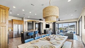 A modern kitchen with a large island, a dining area with a long table, and a living area with a sofa and a large window. - Roof Top Pool at the High Life - 1 Block from the Beach! (Pensacola Beach)