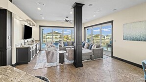 A spacious living area with a large window, a ceiling fan, and a kitchen area with dark cabinetry and a flat-screen TV. - Roof Top Pool at the High Life - 1 Block from the Beach! (Pensacola Beach)
