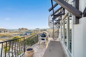 A balcony with a view of the beach, a grill, and a potted plant.