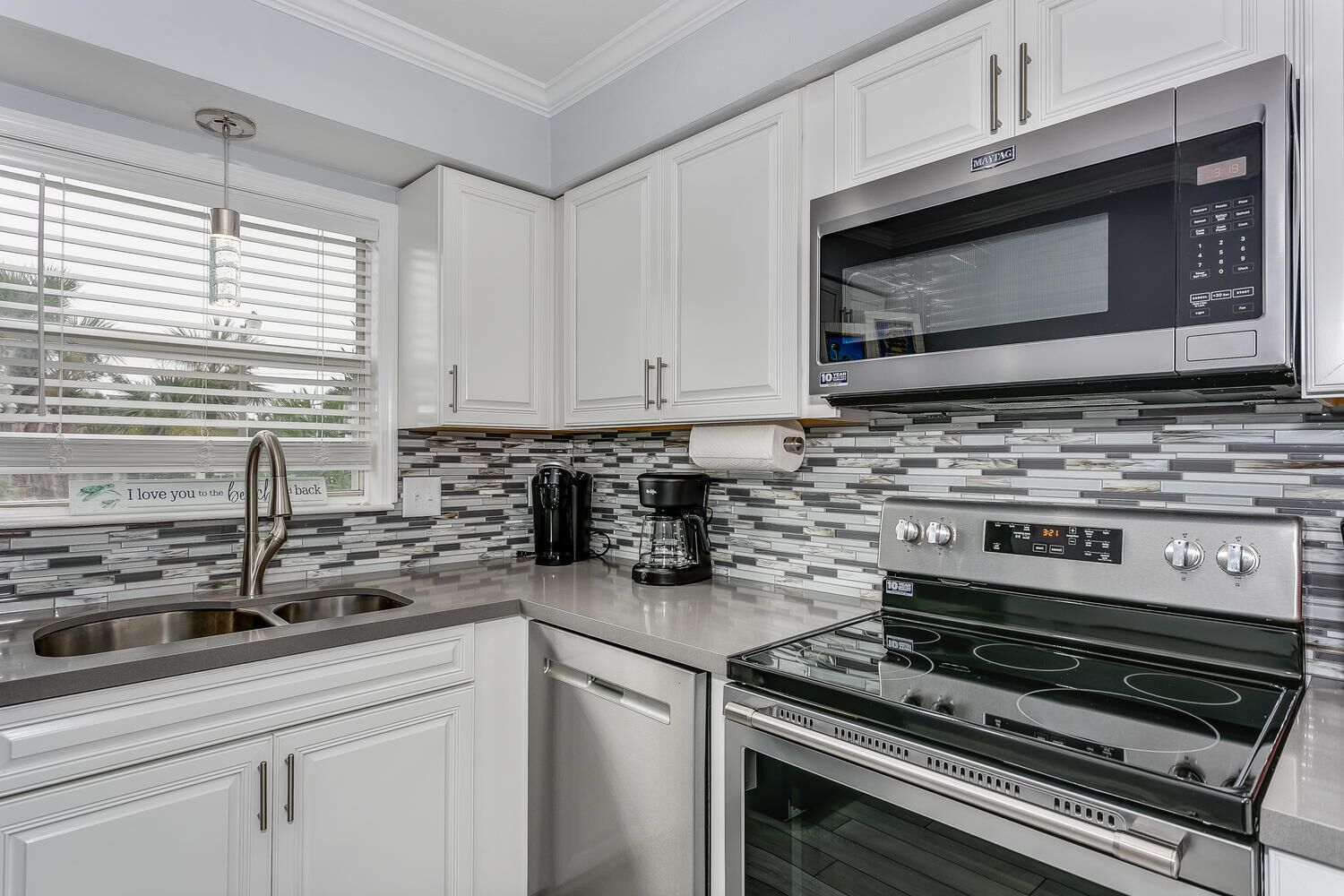 A modern kitchen with white cabinetry, a stainless steel range, a built-in microwave, and a coffee maker.