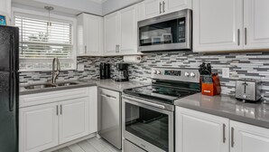 Una cocina moderna con muebles blancos, electrodomésticos de acero inoxidable, microondas, cafetera y tostadora.