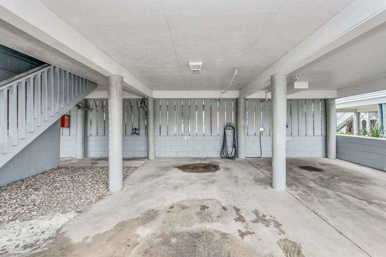 A spacious indoor area with concrete pillars, a staircase on the left, and a hose reel on the right.