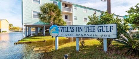A sign for 'Villas on the Gulf' private condominiums with a water body in the foreground.