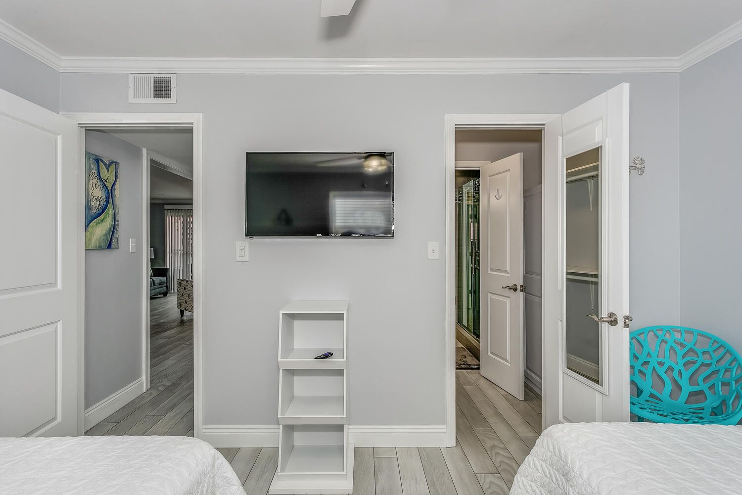 Een slaapkamer met twee bedden, een aan de muur bevestigde televisie en een klein wit plankje.