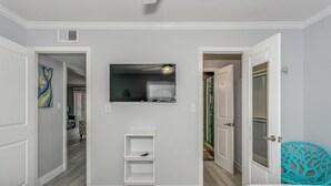 Un dormitorio con dos camas, un televisor montado en la pared y un estante blanco pequeño.