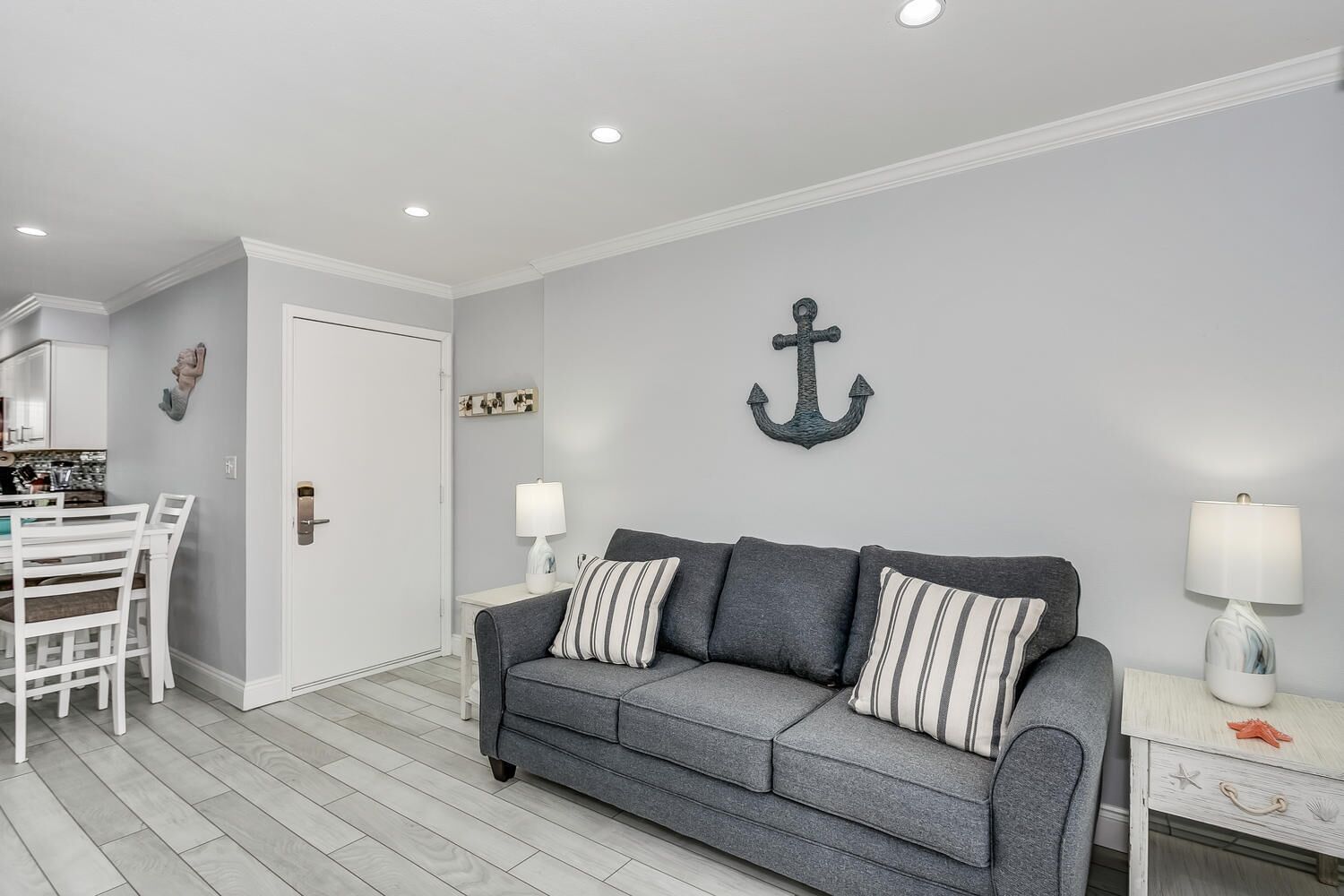 A modern living room with a grey sofa, striped pillows, a white side table with a lamp, and a wall-mounted anchor decoration.