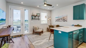 Een moderne keuken met een groot eiland, blauwgroene kastjes en uitzicht op buiten.