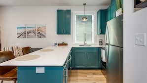 Een moderne keuken met turquoise kastjes, een centraal eiland, roestvrijstalen apparatuur en een eethoek met een houten tafel en stoelen.